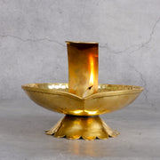 Gold candle holder with a lit candle on a gray background
